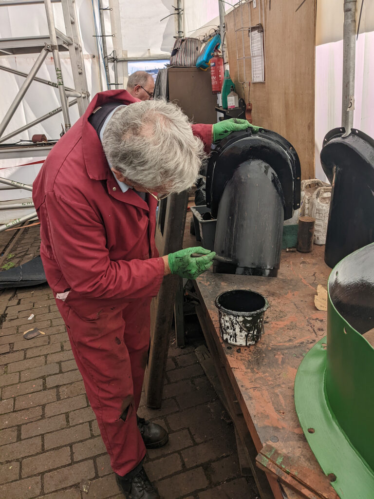 Gloss painting a section of steam pipe cladding, with a piece of firebox cladding in the foreground having already had green undercoat applied.